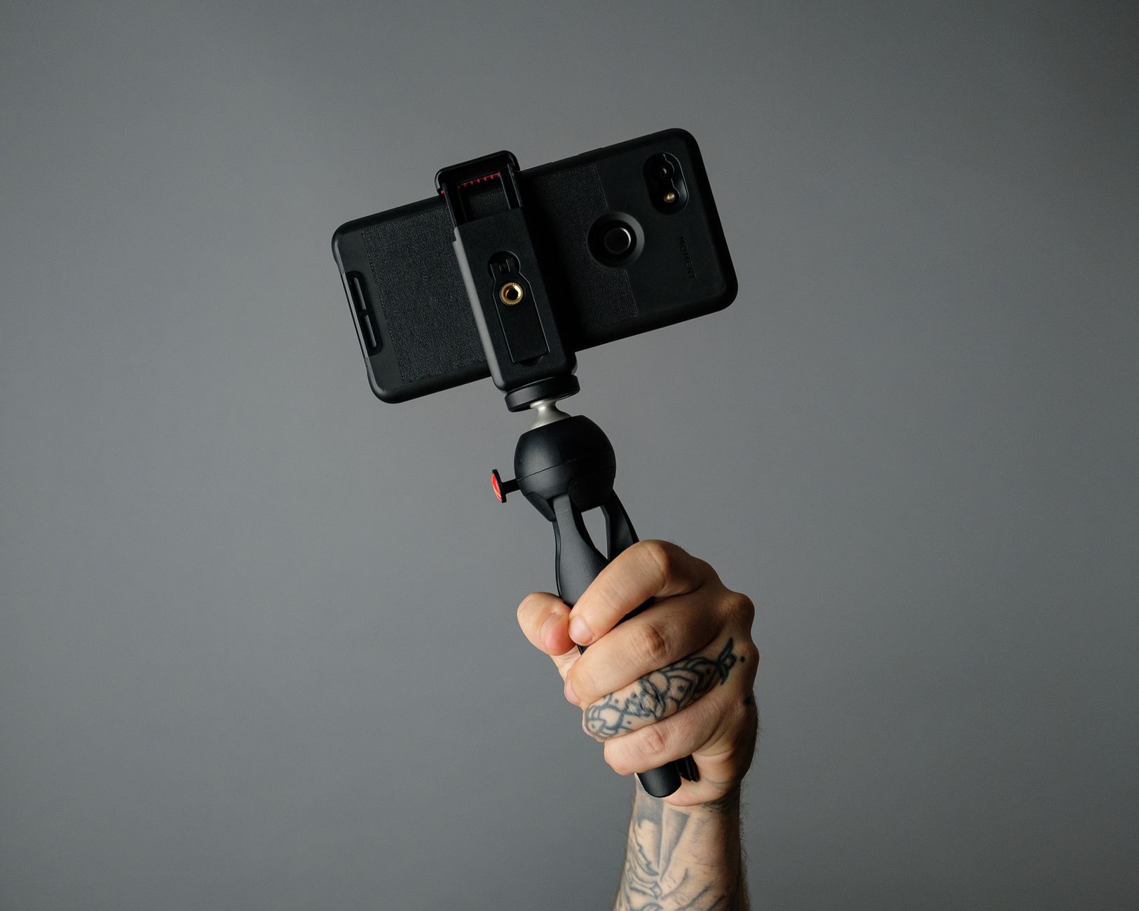 手機錄影教學影片SOP:畫面錄製、投影片與畫中畫實作指南 Tattooed hand holding a smartphone on a gimbal against a neutral background. Perfect for content creation content.