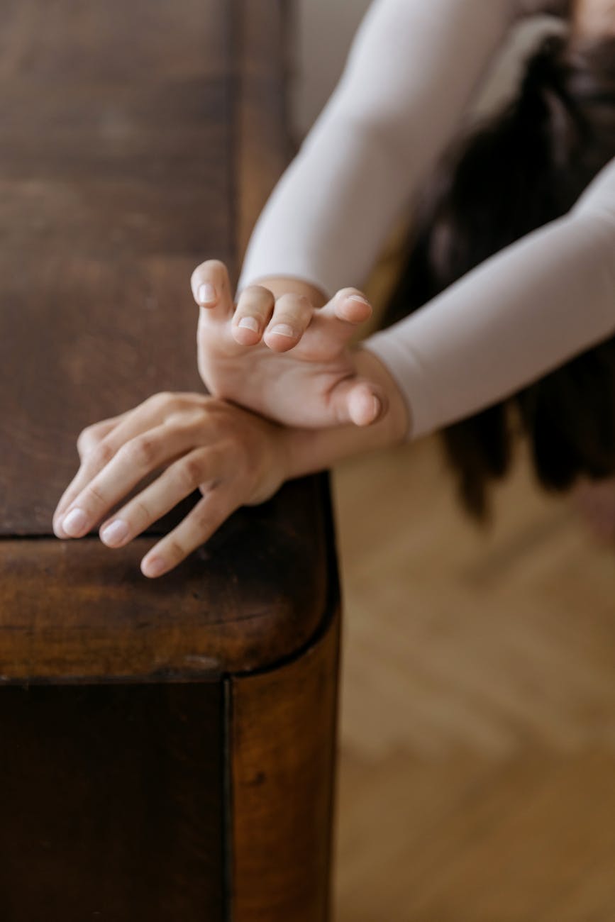 Close-up of two hands resting on a wooden table corner, showing minimalistic and warm tones.