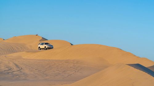 Free Modern off road vehicle driving on sandy dunes in arid hot desert under blue sky Stock Photo