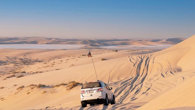 Off road car with flag driving on endless sandy terrain towards mirage and range of dunes