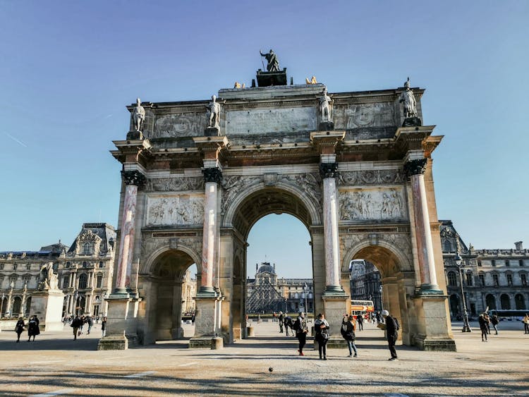 Old Triumphal Arch With Sculptures On Square With Unrecognizable Tourists