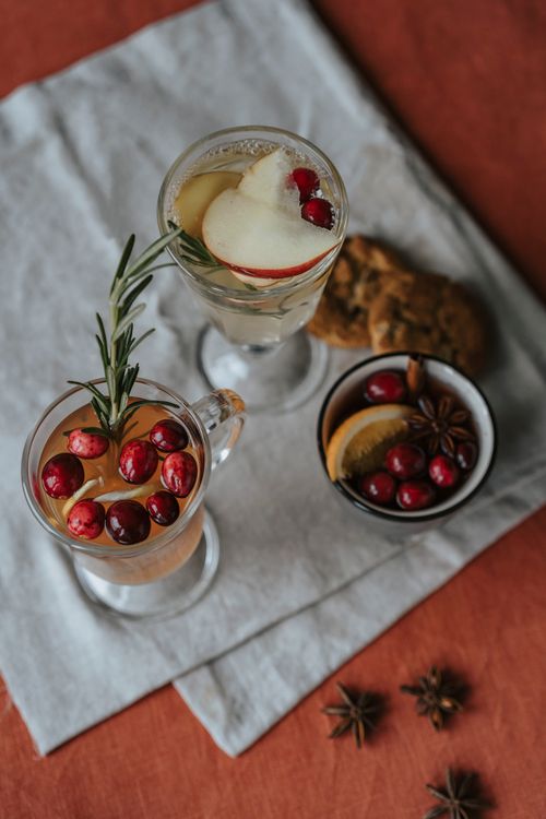 Free Close-up of festive beverages garnished with spices, fruits, and herbs on a linen cloth. Stock Photo