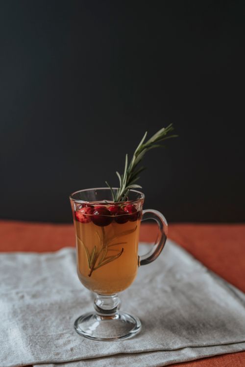 Free Hot cranberry drink with rosemary garnish on a cloth, perfect for cozy winter evenings. Stock Photo