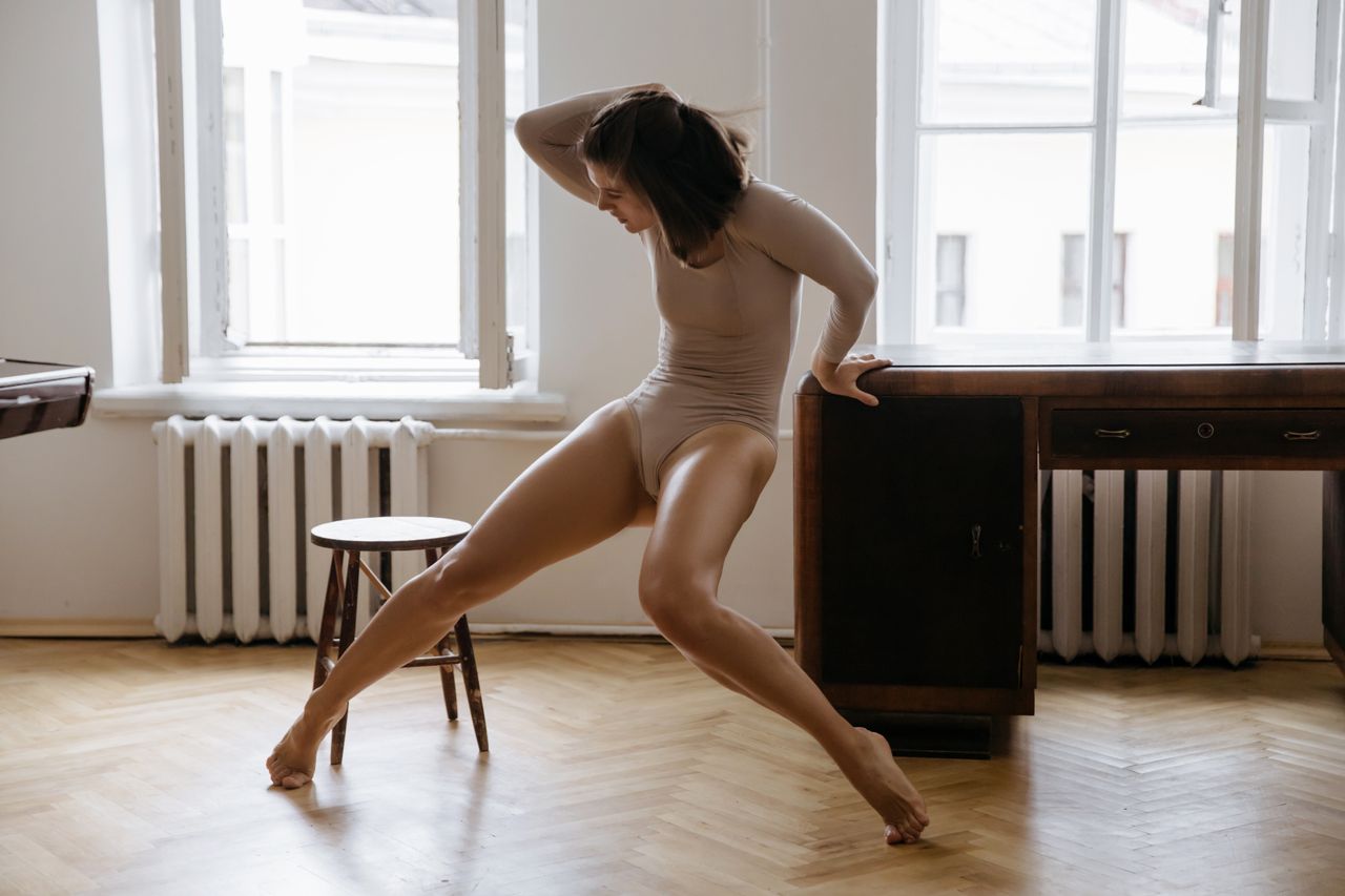 a woman elegantly leans in a dance pose on a wooden floor indoors expr