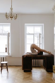 一名女子在光线充足的房间里，于桌旁展示瑜伽姿势，房间窗户敞开着