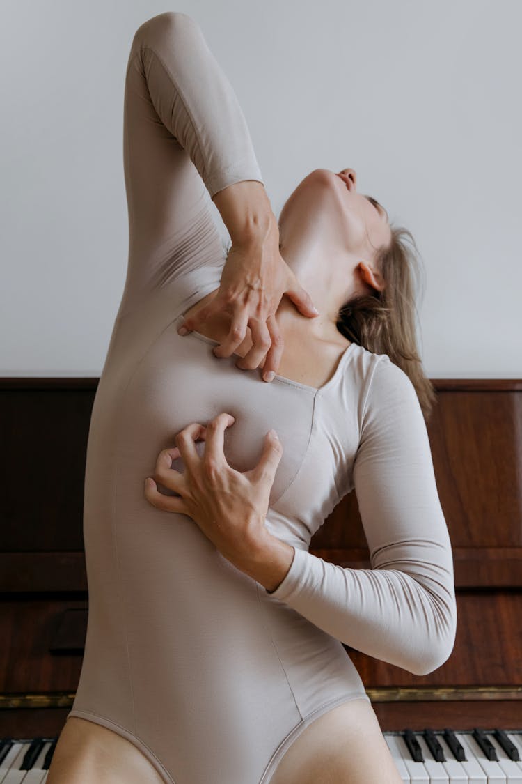 Woman In Beige Bodysuit With Hands On Chest