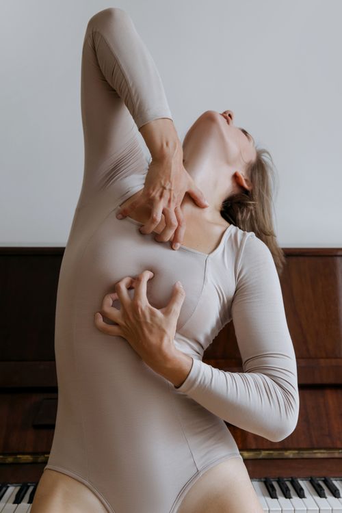 Free Woman in bodysuit expressing emotion through dance in front of piano. Stock Photo