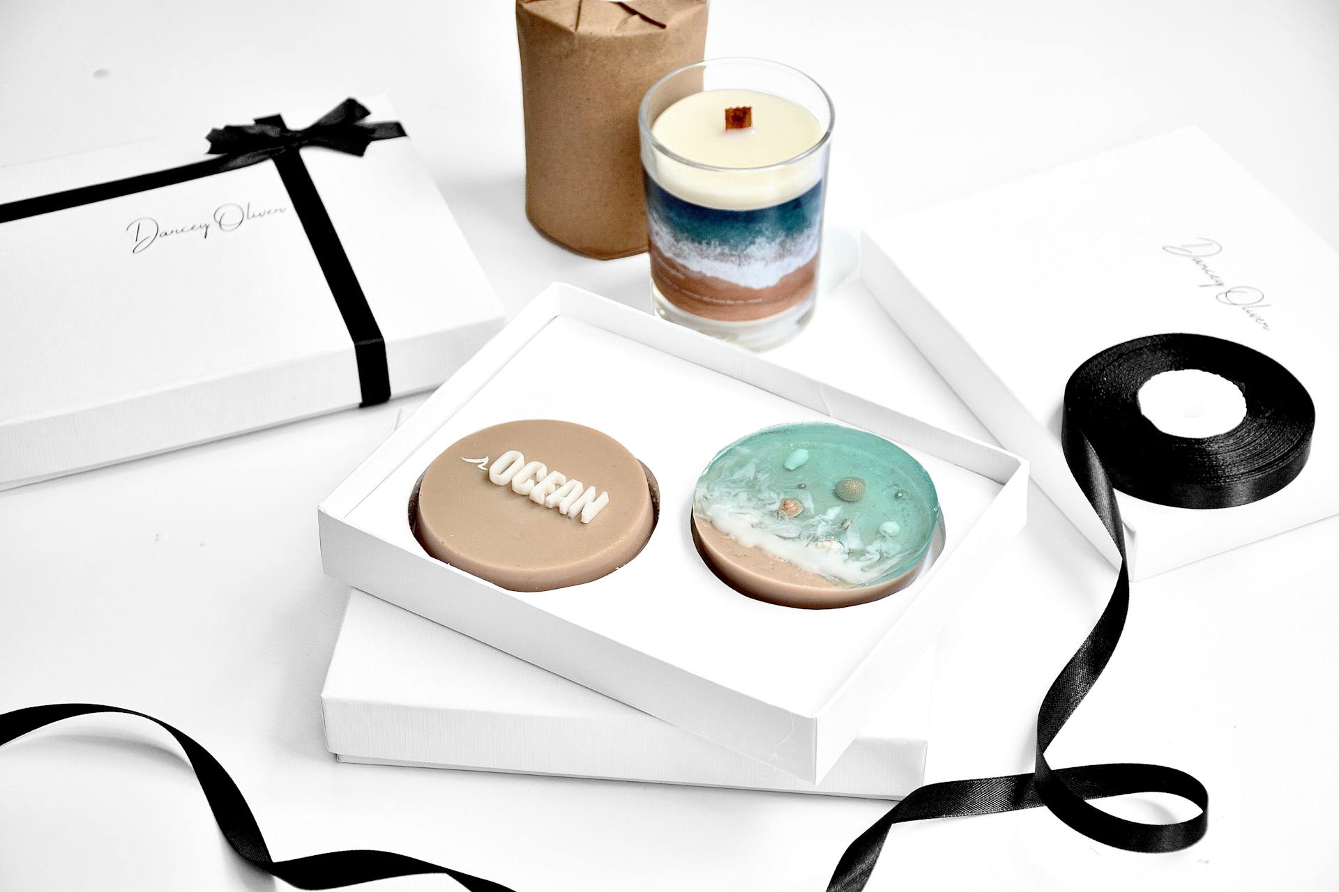 From above of bright round shaped soap with inscription in present box near candle in glass and rolled ribbon