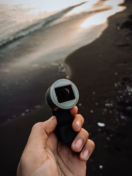 High angle of crop anonymous tourist using portable device for video recording on volcanic beach
