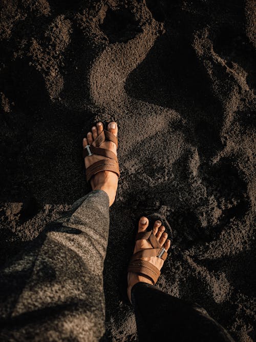 Top view of crop anonymous tourist in sandals standing on shore made of black volcanic mineral rock