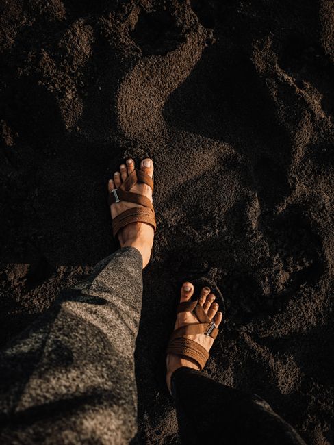 Top view of crop anonymous tourist in sandals standing on shore made of black volcanic mineral rock