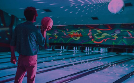 Back view of anonymous male with bowling ball standing near wooden lane with reflection from disco ball at low light