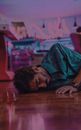 Bearded male with sunglasses wearing shirt lying on floor in shopping center at low light on blurred background