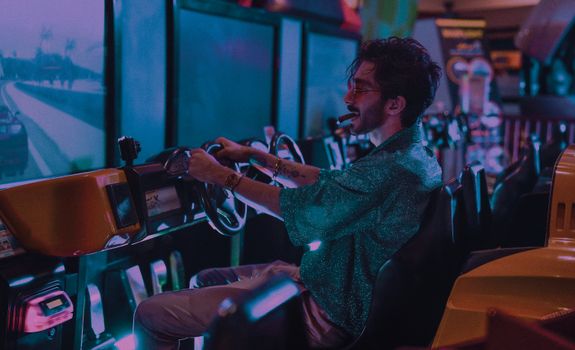 A young man enjoys a racing game at an arcade, immersed in vibrant neon lights.
