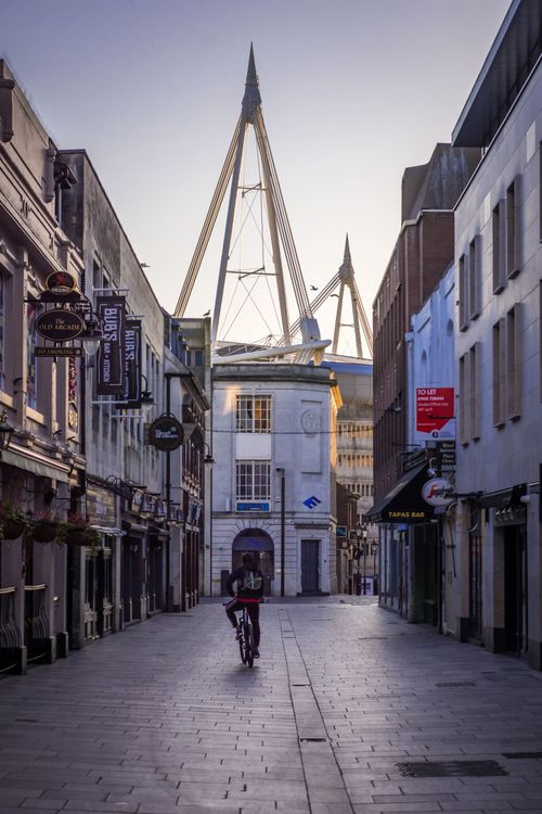 Free A person biking through a quiet street in Cardiff, Wales, with Principality Stadium in the background. Stock Photo