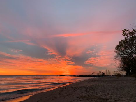 Spectacular scenery of wavy ocean with empty sandy beach against bright cloudy sunset sky