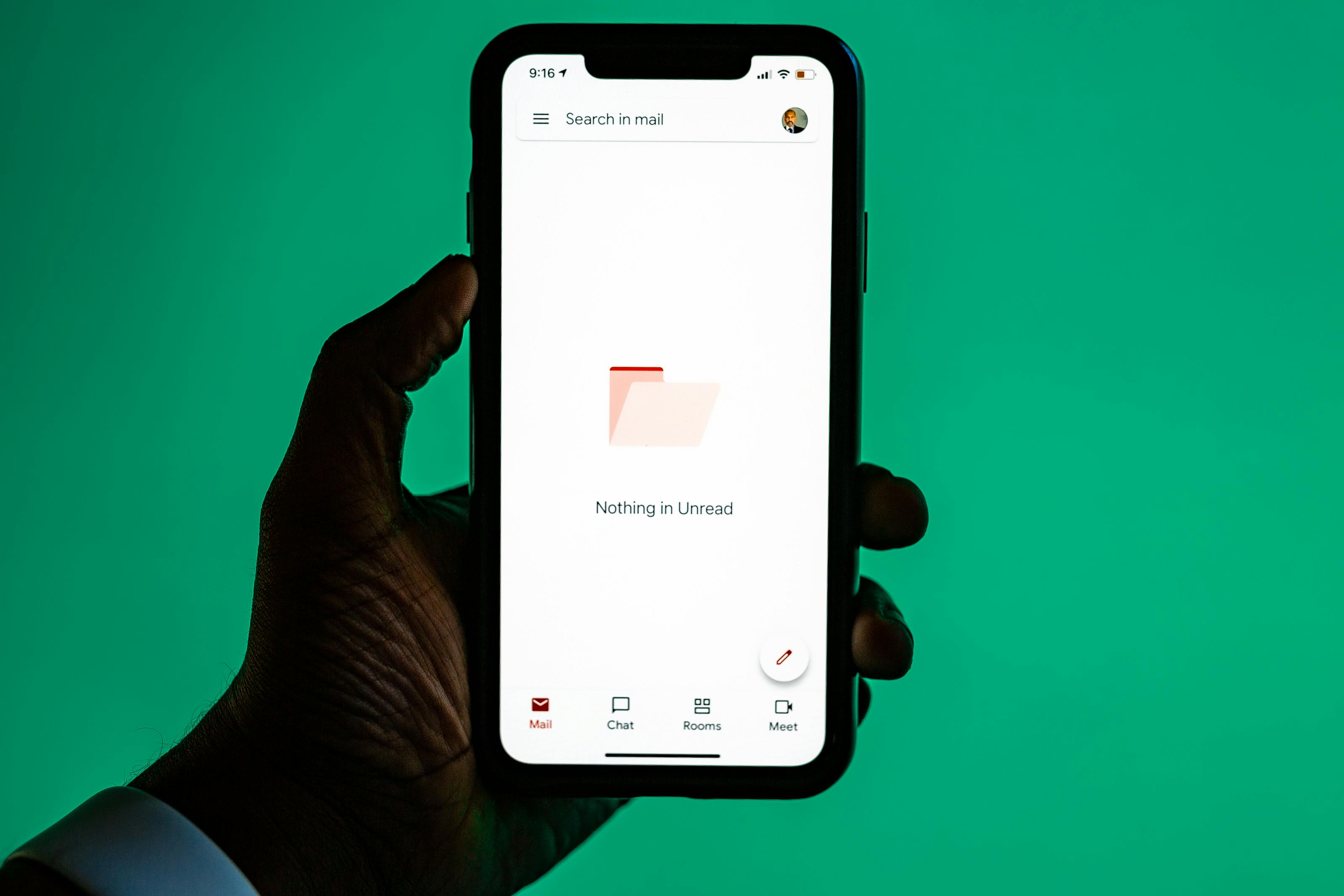 Close-up of a hand holding a smartphone displaying email app against a green background.