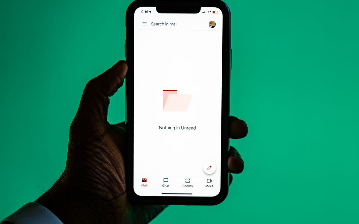 Close-up of a hand holding a smartphone displaying email app against a green background.