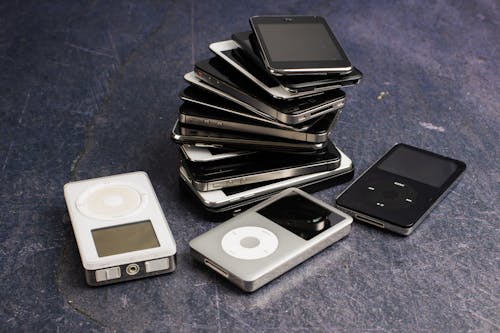 Assorted portable media players and heap of aged cellphones with black screens on gray background