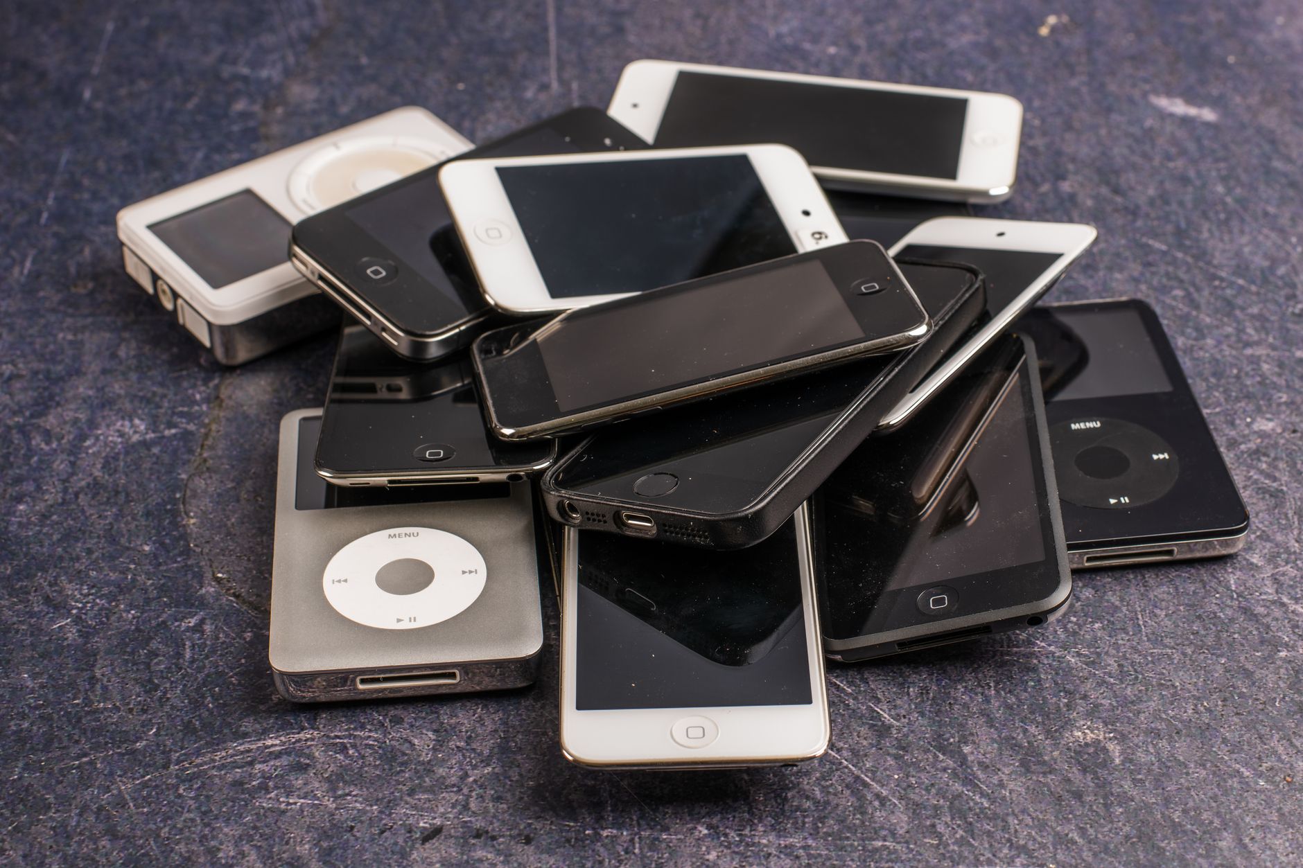 A collection of old MP3 players and smartphones stacked on a table.