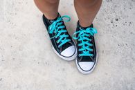 Top view of crop anonymous person in trendy footwear with blue shoelaces on gray background in daytime