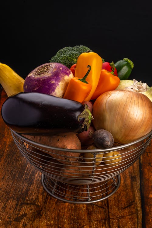 Raw onion near eggplant with bright peppers and broccoli with swede in basket on wooden table