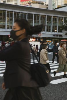 在东京涩谷的一条繁忙街道上，戴着口罩的人们穿行而过，展现了城市生活的景象