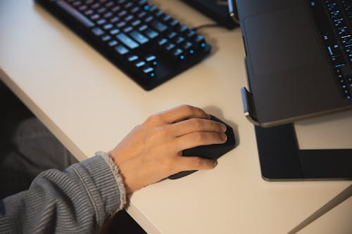 Faceless person working on computer using mouse and keyboard and having laptop on cradle