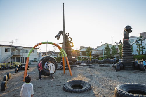 Small yard with huge monster creature figures constructed of old tyres on playground full of children