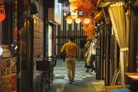 Back view of anonymous man in casual clothes walking along narrow bright street with shops and speaking in phone