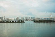 在蓝色多云的天空下，现代城市与桥梁跨越宽阔的河流，连接着摩天大楼