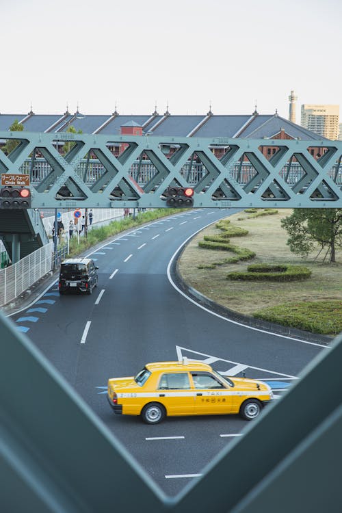 Yellow taxi car driving along asphalt roadway under pedestrian overpass in contemporary city district