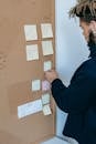 Serious ethnic guy reading sticky notes attached to pinboard