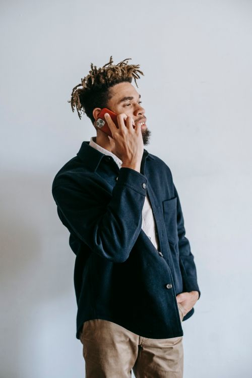 Free Confident young informal African American male in stylish outfit having  phone conversation while standing against white wall with hand in pocket Stock Photo
