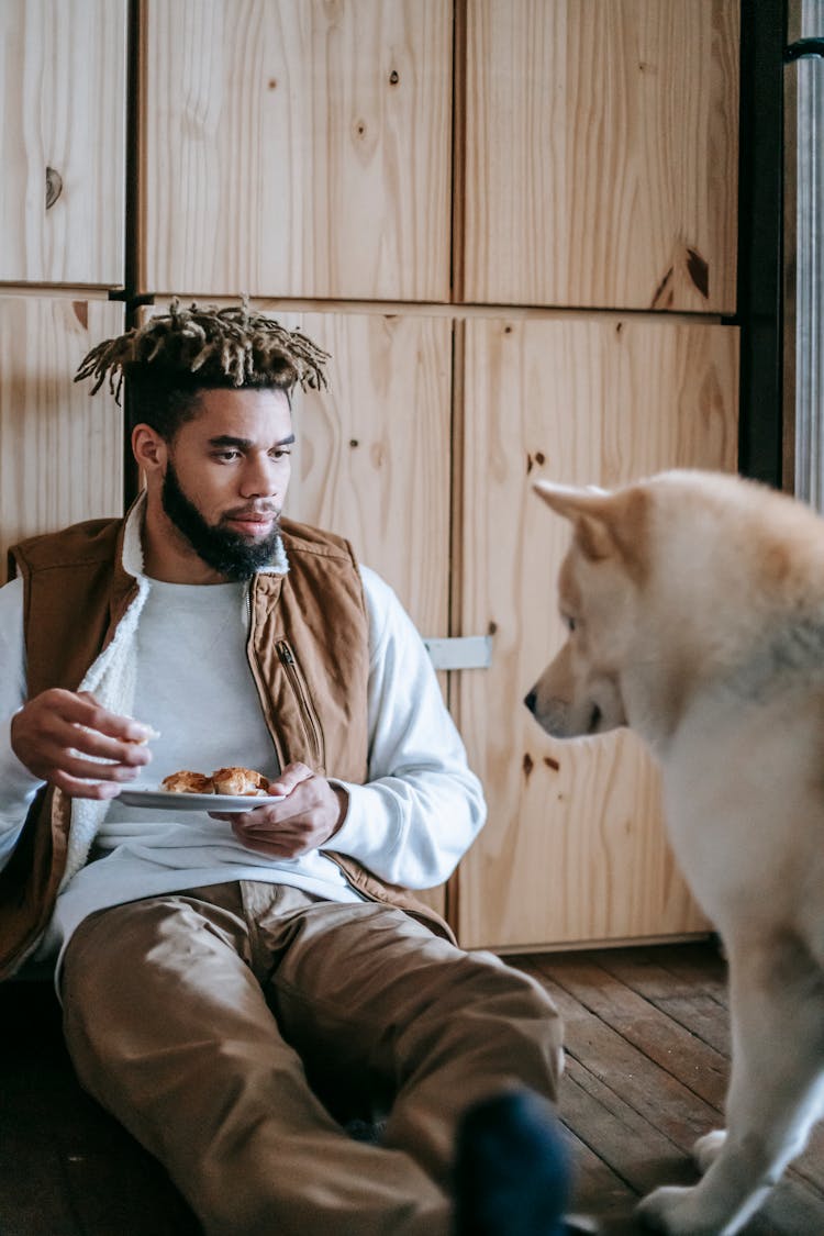 Young Black Male Eating Croissant Near Adorable Purebred Dog