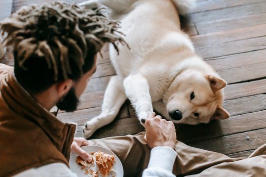 一名留着辫子的男子和他的秋田犬在木地板上分享羊角面包，描绘了友谊与纽带