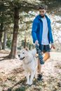 Young attentive bearded ethnic male with dreadlocks and scarf taming fluffy dog with tongue out in sunlight