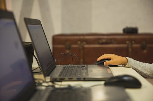 Crop anonymous schoolkid against open netbook with information on screen studying at table in classroom