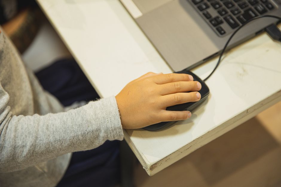 屋内でオンライン学習のためにノートパソコンとマウスを使用する子供の手のクローズアップ。