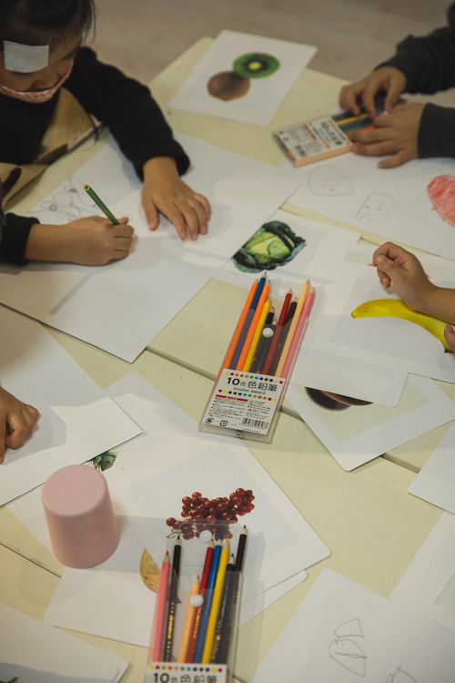 Free From above of anonymous ethnic kids drawing with colored pencils on papers during COVID 19 pandemic in kindergarten Stock Photo