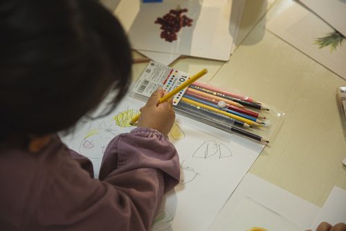 Free High angle of crop anonymous preschool ethnic kid coloring drawing on paper sheet during art class Stock Photo