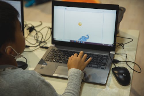 Free From above back view of crop anonymous Asian schoolchild typing on netbook with illustration on screen during lesson in school Stock Photo