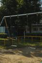 Metal empty swings on playground in yard among green trees on sunny summer day