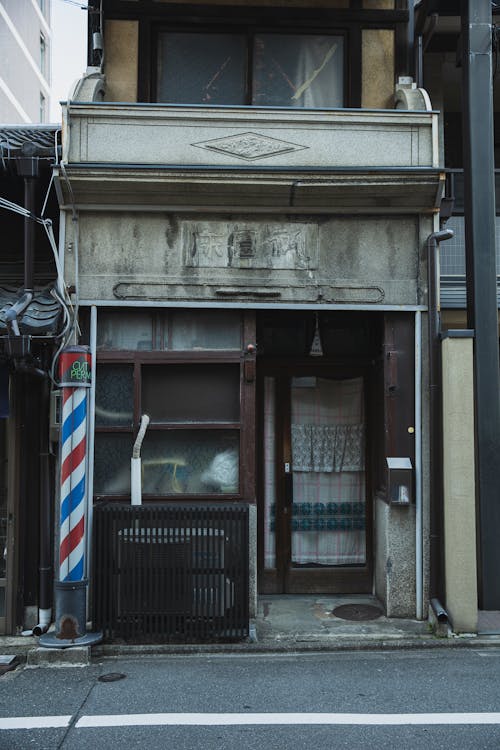 Aged weathered gray entrance of barbershop on street with asphalt road in daytime