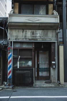 白天，柏油路旁的理发店入口老旧风化，呈现灰色