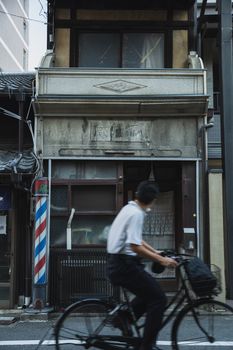 A cyclist rides past a traditional barber shop in Kyoto, Japan, showcasing a blend of motion and culture.
