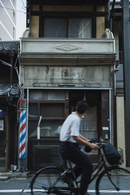 Free A cyclist rides past a traditional barber shop in Kyoto, Japan, showcasing a blend of motion and culture. Stock Photo