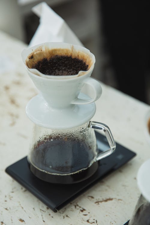 From above of fresh aromatic coffee using filter dripper placed on white wooden table at home in daytime