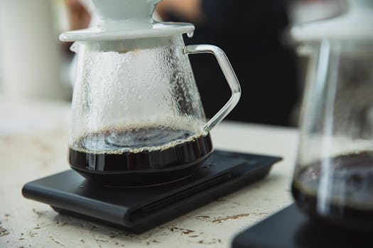 Glass coffee pot with fresh brew on digital scale, capturing modern café vibe.