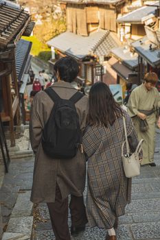 一对身着时髦服装的匿名夫妇，在传统建筑之间的人行道上漫步的背影